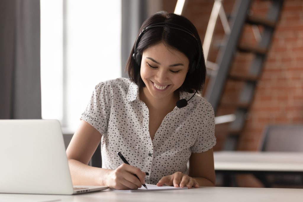 Happy,Asian,Businesswoman,Wearing,Headset,Make,Notes,Talk,By,Conference